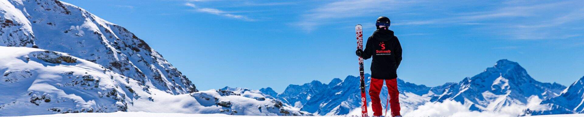 Un guide Sunweb avec des skis Sunweb face aux montagnes enneigées