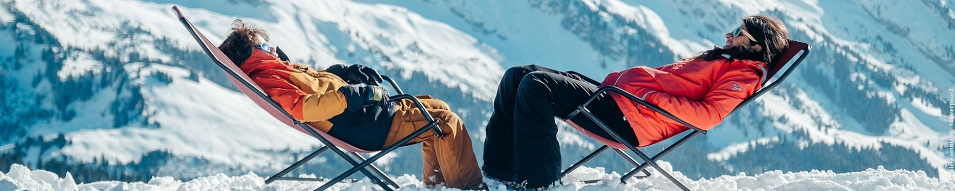 Deux personnes sur un transat au ski avec les montagnes en arrière-plan