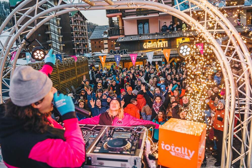 Un DJ chantant depuis une scène sous une arche métallique face à des étudiants lors d'une fête Totally