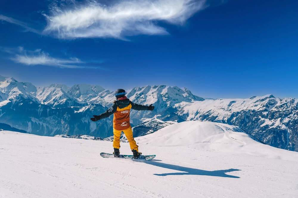 Un snowboarder avec une veste de ski Totally descendant les pistes en snowboardant les bras écartés