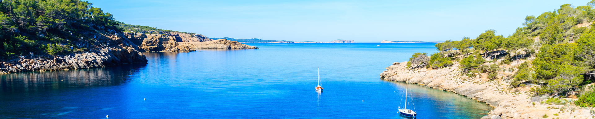 Plage avec bâteaux , entourée de rochers verdoyants, Ibiza, Espagne