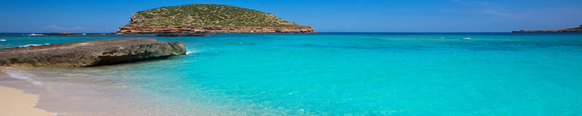 Plage de sable fin aux eaux cristallines et rocher imposant, last minute Ibiza, Espagne