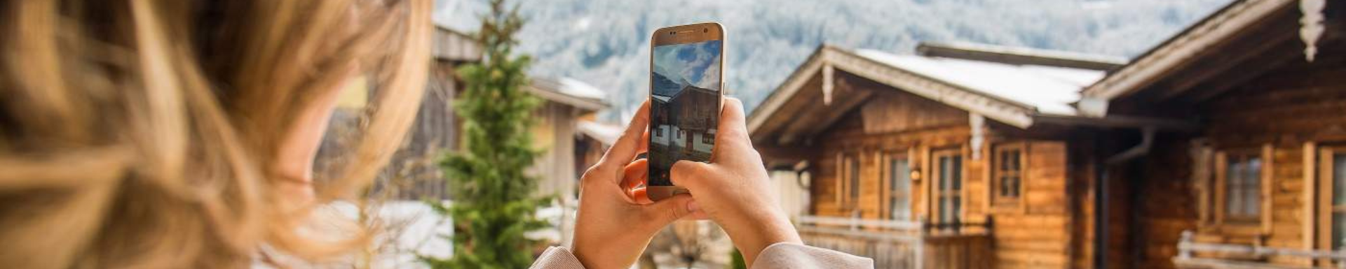 Une femme de dos prenant en photo un chalet en bois au ski