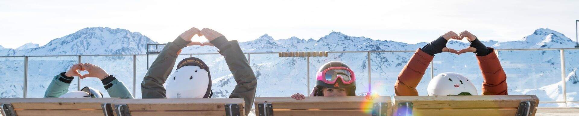 Une famille assises de dos faisant un coeur avec leurs mains, face à la montagne